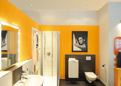 Ein Mann mit pinkem Haar und einer Sonnenbrille, der vor einem grauen Hintergrund steht und in die Kamera schaut.